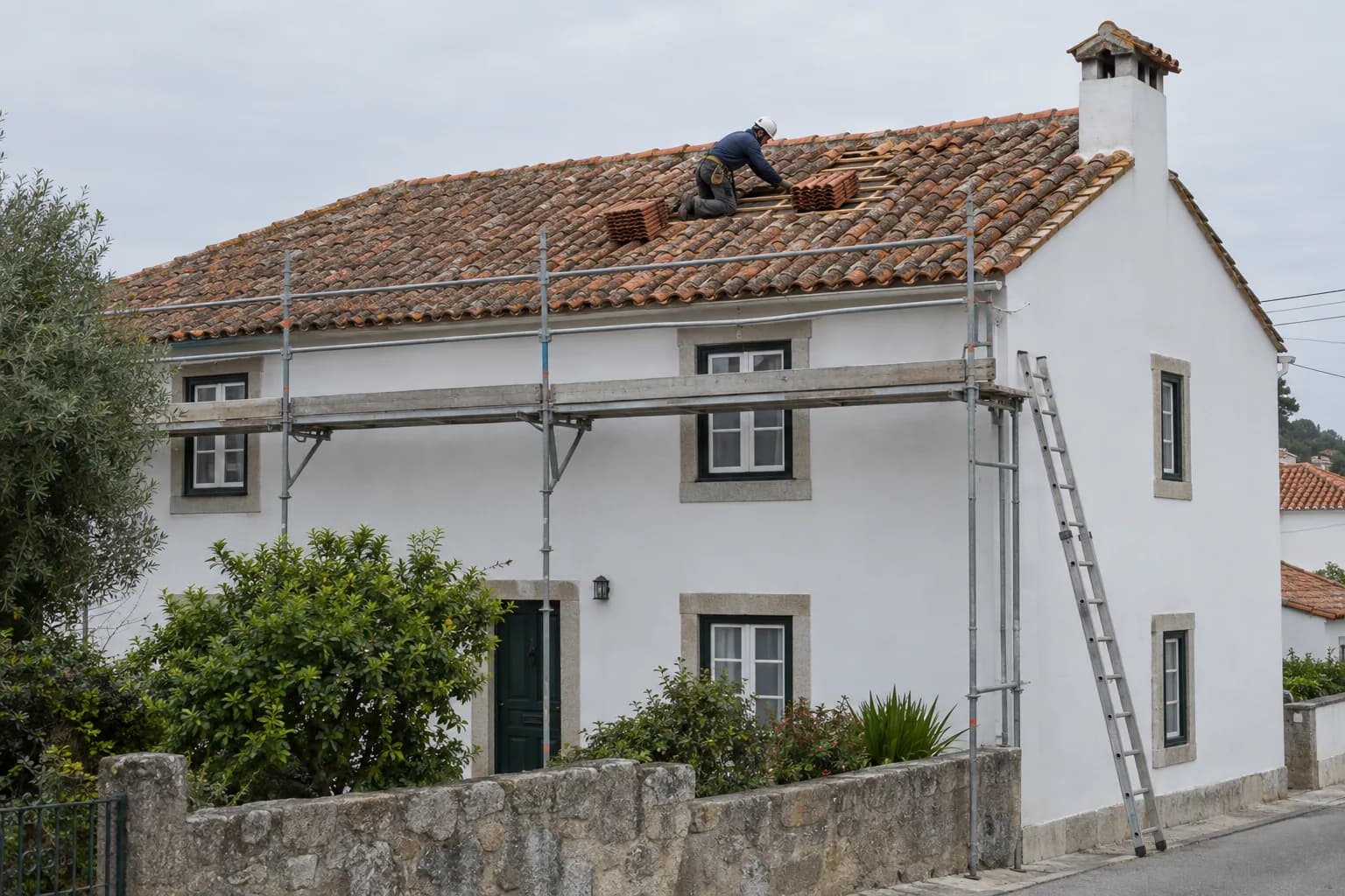 Casa rendida com telhado de telha cerâmica, andaime no beiral e um telhador a substituir telhas